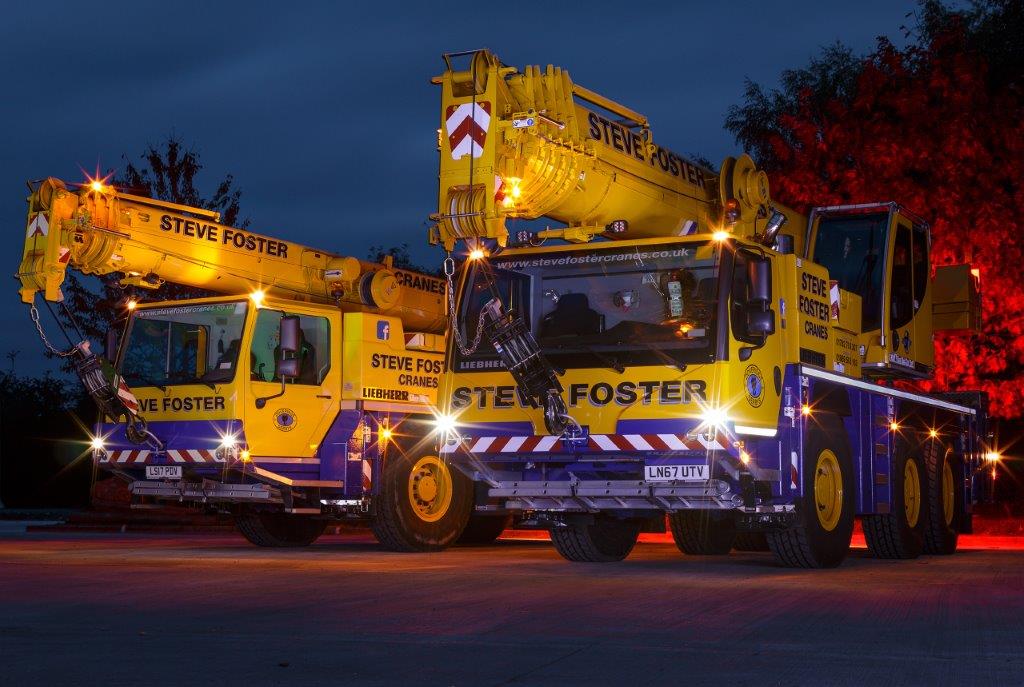 Two Steve Foster Cranes yellow mobile cranes illuminated at dusk